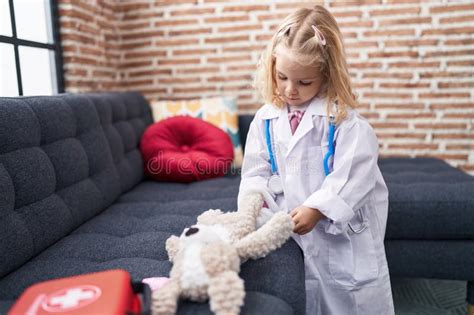 Adorable Blonde Girl Student Writing On Notebook Sitting On Table At Classroom Stock Photo