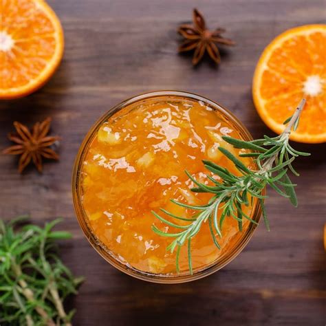 An Orange Drink With Rosemary Garnish In A Glass On A Wooden Table