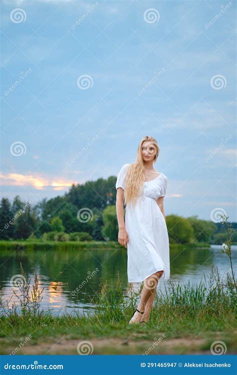 Portrait Of A Cute Girl In A White Dress On The River Bank During