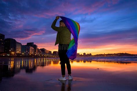 Asombrosa Foto De Un Joven Parado En La Playa Y Sosteniendo En Las Manos Una Bandera Gay Foto De