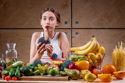 Hungry Woman Eating Black Burger At The Table Full Of Fruits And