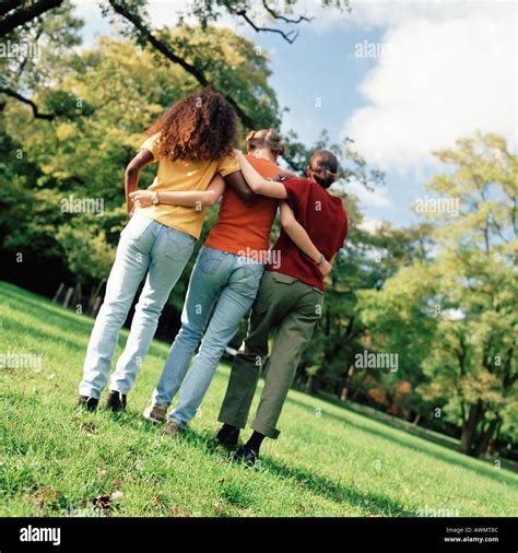 Three Young Women Walking On Grass With Arms Around Each Other Rear View Full Length Stock