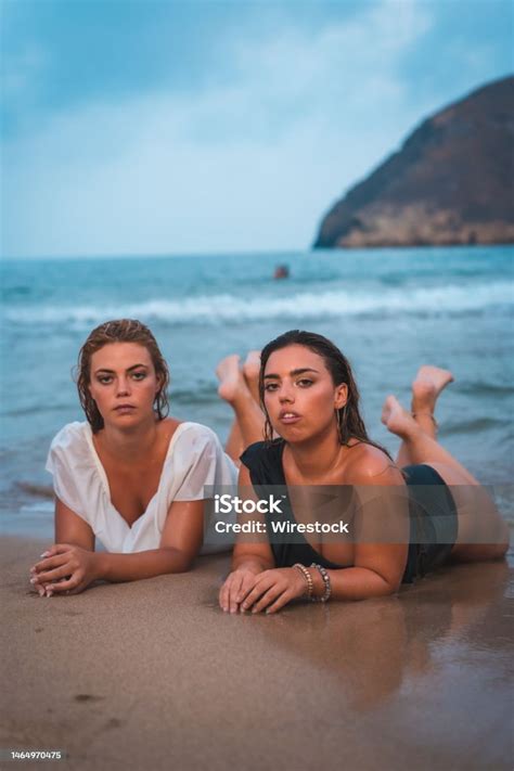 Beautiful Caucasian Lesbian Couple In Swimsuits Lying On The Sand With The Sea In The Background