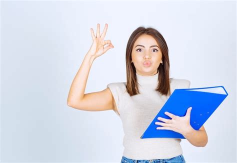 Modelo De Mujer Joven Sosteniendo Una Carpeta Azul Y Mostrando Gesto Ok