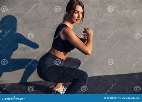 Sportive Woman In Sneakers And A Tracksuit Squatting Doing Squats On