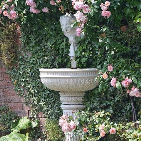 A Garden Fountain Surrounded By Pink Flowers And Greenery