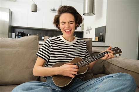 Niña hermosa tocando el ukelele en el sofá cantando su canción favorita