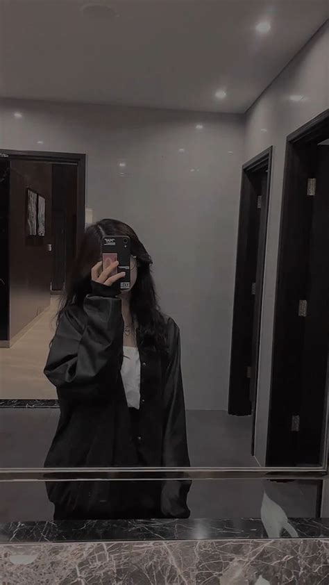 A Woman Taking A Selfie In Front Of A Mirror While Wearing A Black Jacket