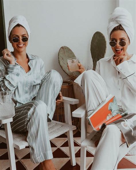 Two Women Sitting On Chairs Wearing White Robes And Holding Coffee Mugs