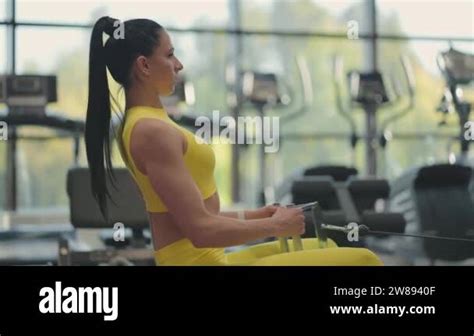 Hispanic Woman Does Exercises On The Rowing Machine A Girl Sits Behind