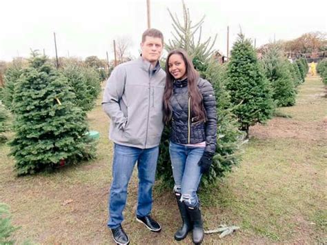 A Man And Woman Standing Next To Each Other In Front Of Trees At A