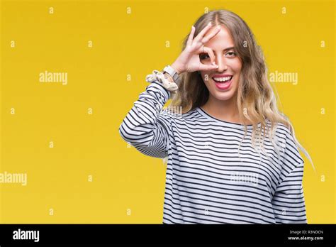 Schöne junge blonde Frau mit Streifen Pullover über isolierte Hintergrund tun ok Geste mit der