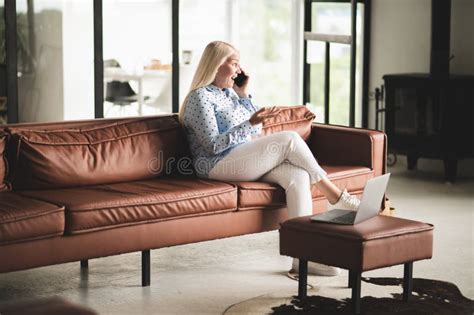 Blonde Mature Woman Talking On The Phone While Sitting On The Sofa Stock Photo Image Of