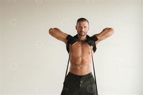 A Man With A Naked Torso Is Engaged In Strength Fitness Using A Rubber Loop Indoors 39904396