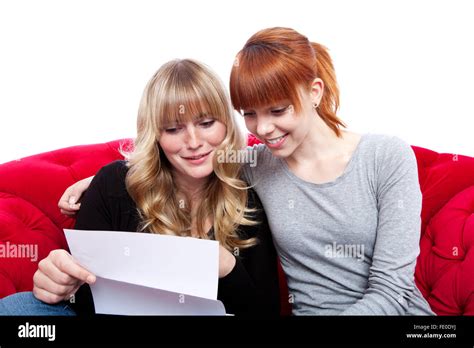 schöne junge blonde und rote behaarte Mädchen auf roten Sofa lesen Buchstaben vor weißem