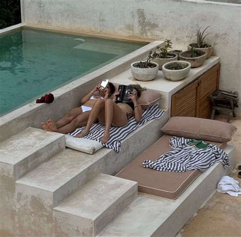 Two Women Lounging On Loungers In Front Of A Swimming Pool With Their