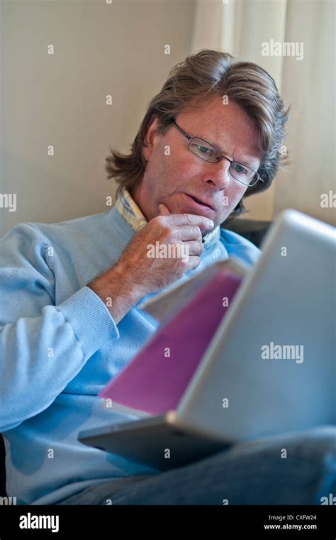 Mature Man At Home Checking Business Paperwork Using His Laptop