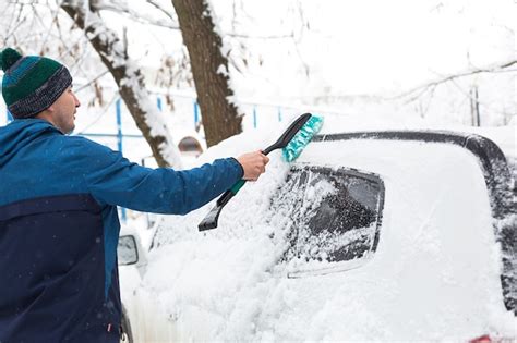 Premium Photo A Man Brushes Snow From A Car After A Snowfall