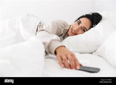 Photo Of Brunette Woman 30s Using Smartphone While Lying In Bed With White Linen At Home Stock