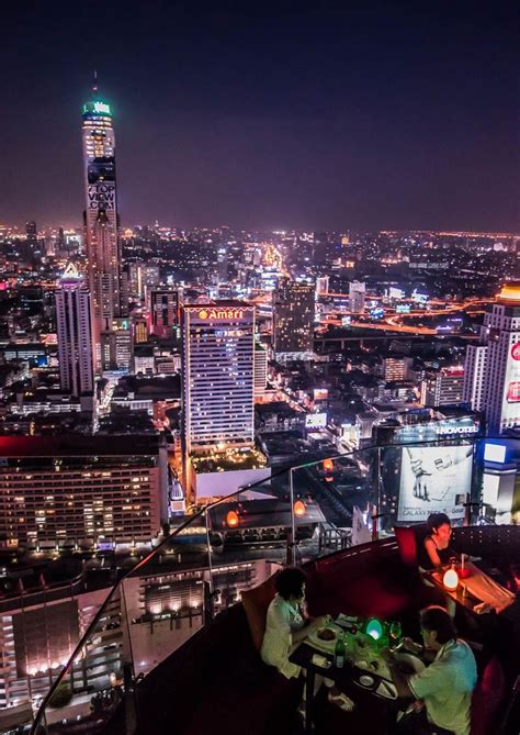 a man sitting at a table on top of a tall building with city lights in ...