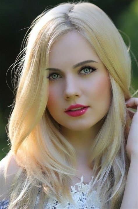 A Woman With Long Blonde Hair And Blue Eyes Posing For A Photo In Front Of Trees