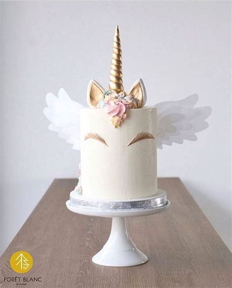 A White Cake Topped With A Unicorn S Head And Wings On Top Of A Wooden