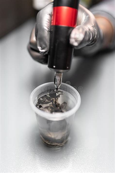 Close Up Of A Tattoo Artist Is Pouring Ink Into A Plastic Glass To