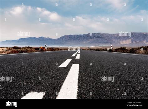 Long Straight Empty Asphalt Road Through Arid Landscape Against Ocean