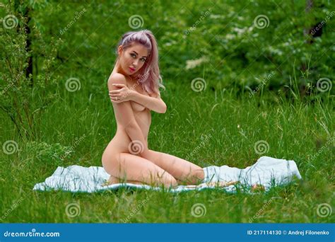 Charming Nude Blonde Posing While Sitting On A Bedspread On A Green Lawn In A Summer Forest