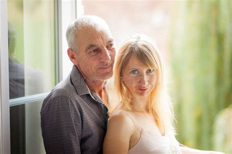 Homme Supérieur étreignant Sa Jeune épouse Blonde Près De La Fenêtre Femme Regardant L appareil