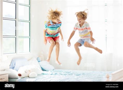 Child jumping on bed in white bedroom with big window. Kids play at ...