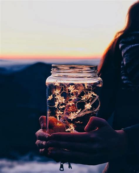 A Person Holding A Jar Filled With Flowers In Front Of A Mountain Range