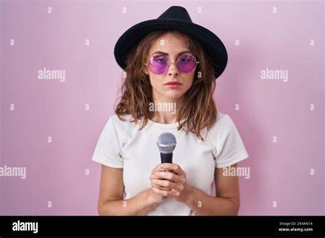 Beautiful Brunette Woman Singing Song Using Microphone Relaxed With Serious Expression On Face