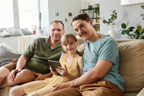 Retrato de familia gay feliz sonriendo a la cámara mientras está sentado en el sofá con el niño