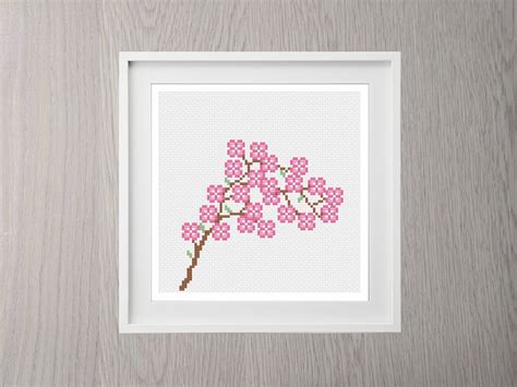 A Cross Stitch Cherry Blossom Is Displayed In A White Frame On A