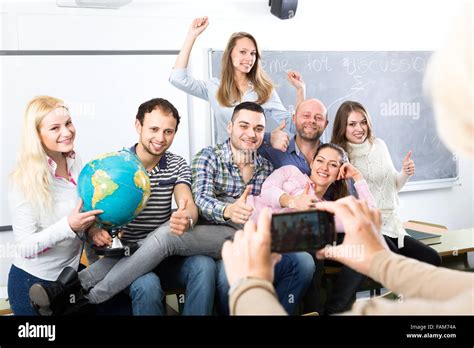 Le professeur mature de prendre une photo de ses diplômés dans une salle de classe avec son