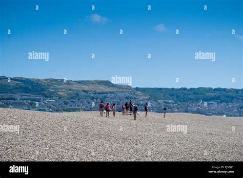 People Walking Along The Pebbled Tombolo Of Chesil Beach With The Isle