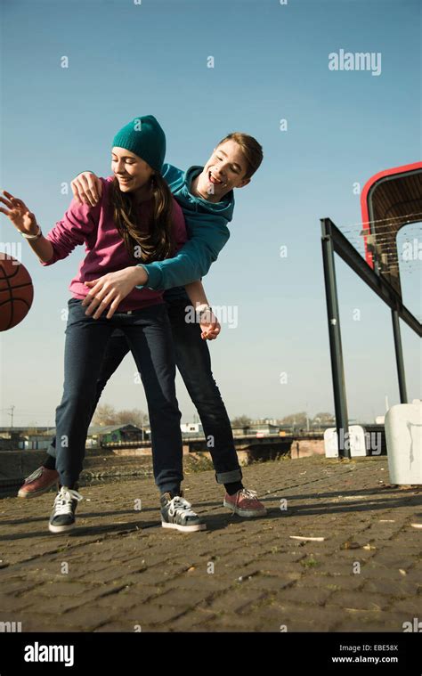 Teenage boy and girl playing basketball outdoors, industrial area ...