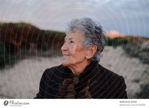 Positive Senior Woman Smiling While Resting On Sandy Seashore In