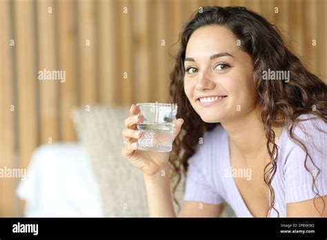 Happy Woman Holding Water Glass Looks At You Sitting On A Bed Stock