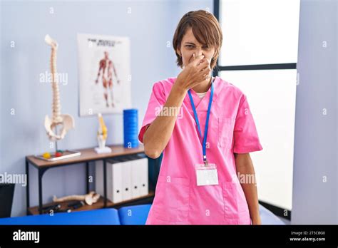 Brunette Woman Working At Rehabilitation Clinic Smelling Something Stinky And Disgusting