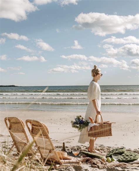 A Woman Walking On The Beach Carrying A Wicker Basket With Flowers In