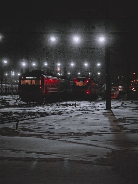 Two Trains Are Parked At The Train Station In The Snow With Lights