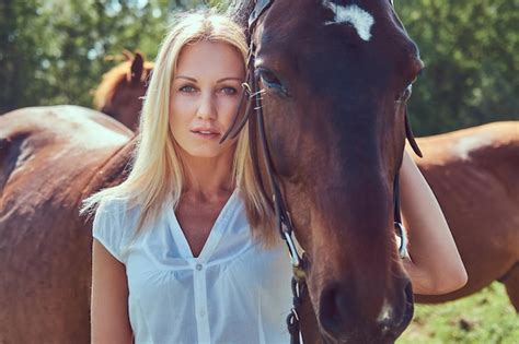 Charmante belle blonde vêtue d un chemisier blanc et d un jean serrant un cheval dans un champ