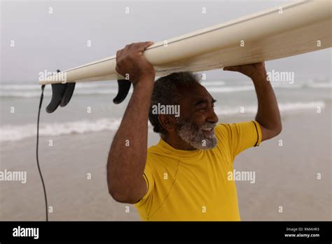 Senior Male Surfer Carrying The Surfboard On His Head At Beach Stock