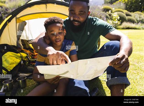 happy african american father  son sitting  grass  reading map