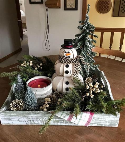 A Snowman Sitting On Top Of A Table Next To Pine Cones And Evergreens