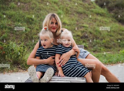 Une jeune fille blonde excitée est assise sur un banc en béton dans le parc avec sa mère et sa