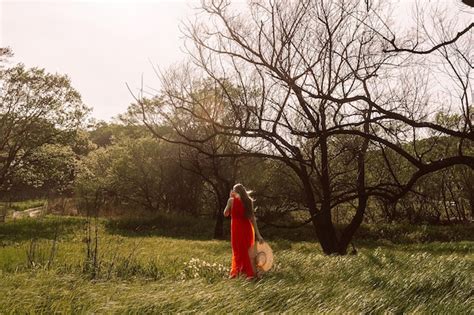 Una mujer con un vestido rojo se encuentra en un campo con un árbol al