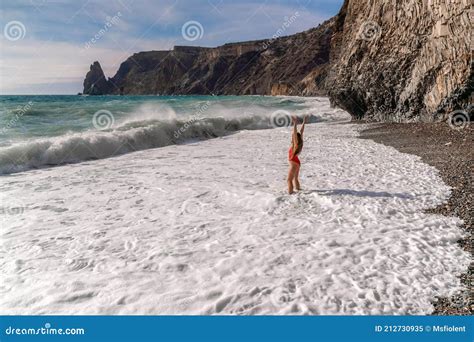 A Beautiful And Brunette In A Red Swimsuit On A Pebble Beach Running Along The Shore In The